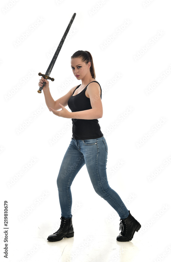 full length portrait of brunette girl wearing black single and jeans. standing pose holding a sword. isolated on white studio background. full length portrait of brunette girl wearing black single and jeans. standing pose holding a sword. isolated on white studio background.