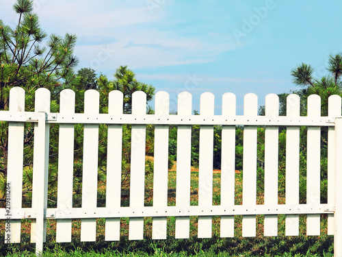 White wooden fence on green grass against of the blue sky. © zurbagan
