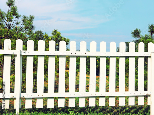 White wooden fence on green grass against of the blue sky.