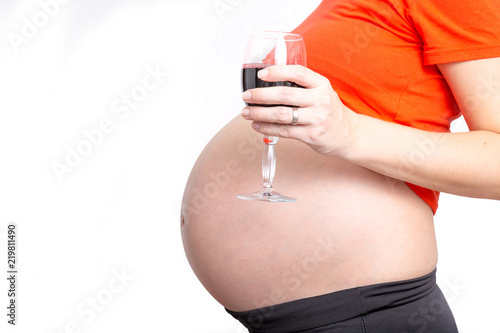 Pregnant woman with a glass of wine on the stomach seating on the couch, concept of unhealthy lifestyles during pregnancy and motherhood.