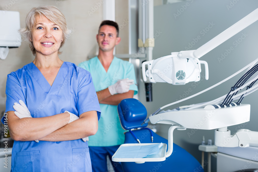 Fototapeta premium Portrait of friendly woman dentist arms crossed with dental assistant behind