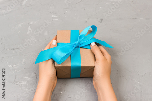 Female hands holding craft gift box with blue ribbon on gray background photo