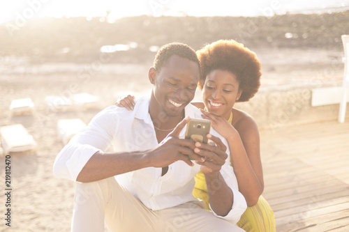 young happy couple afroamerican afro race multiethnic racial diversity enjoy phone and internet in outdoor leisure activity during the bright and golden sunset with light in background.  © simona