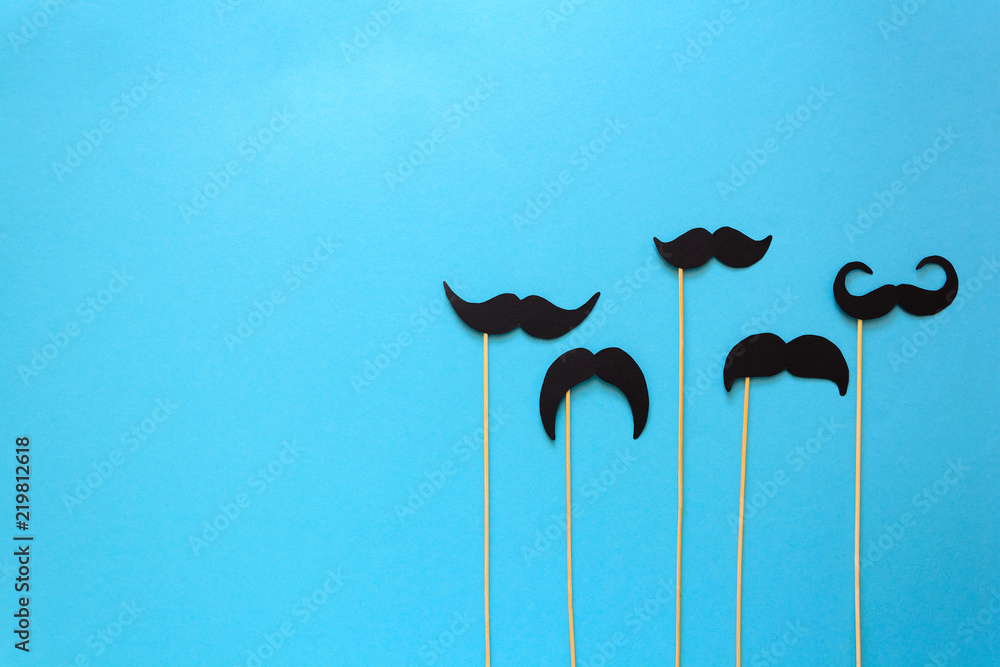 Paper mustache on booth props on blue paper background. Cut out style. Movember concept. Top view. Flat lay. Copy space - obrazy, fototapety, plakaty 