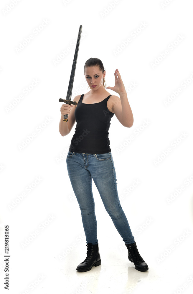 full length portrait of brunette girl wearing black single and jeans. standing pose holding a sword. isolated on white studio background. full length portrait of brunette girl wearing black single and jeans. standing pose holding a sword. isolated on white studio background.