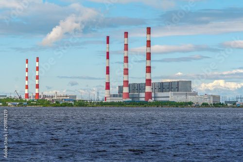 Thermal power plants with bright chimneys on the shore of the reservoir in a bright sunny day.