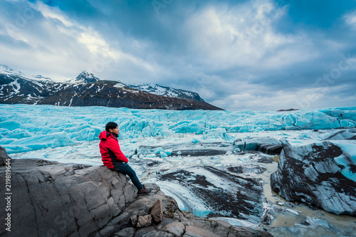 Asian young man in red jacket looking the glacier in iceland