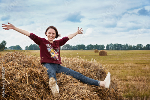 young girl having fun in the field, sitting on a haystack