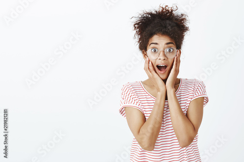 Wow, amazing news. Surprised happy attractive curly-haired woman in trendy glasses and striped t-shirt, shouting and holding hands near mouth while staring with popped eyes at impressive sale