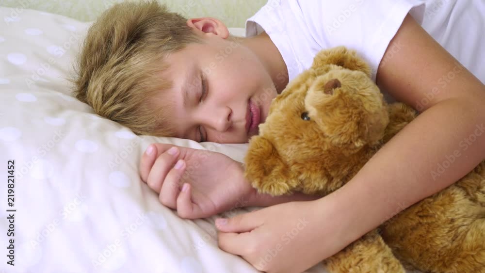 Closeup portrait of cute sleeping calm young white kid lying in his comfortable bed hugging cute brown teddy bear toy. Real time 4k video footage. Closeup portrait of cute sleeping calm young white kid lying in his comfortable bed hugging cute brown teddy bear toy. Real time 4k video footage.