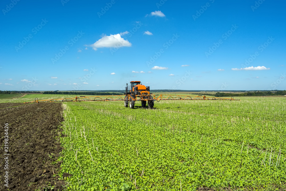 self-propelled sprayer works on a field under a blue sky with clouds self-propelled sprayer works on a field under a blue sky with clouds