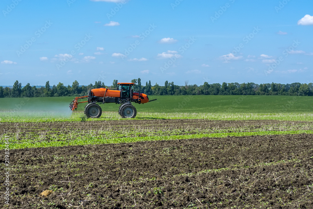 Fototapeta premium self-propelled sprayer works on a field under a blue sky with clouds