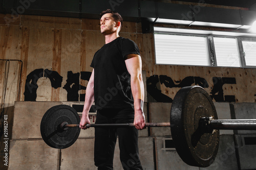 Fit young man lifting barbells, working out in a gym