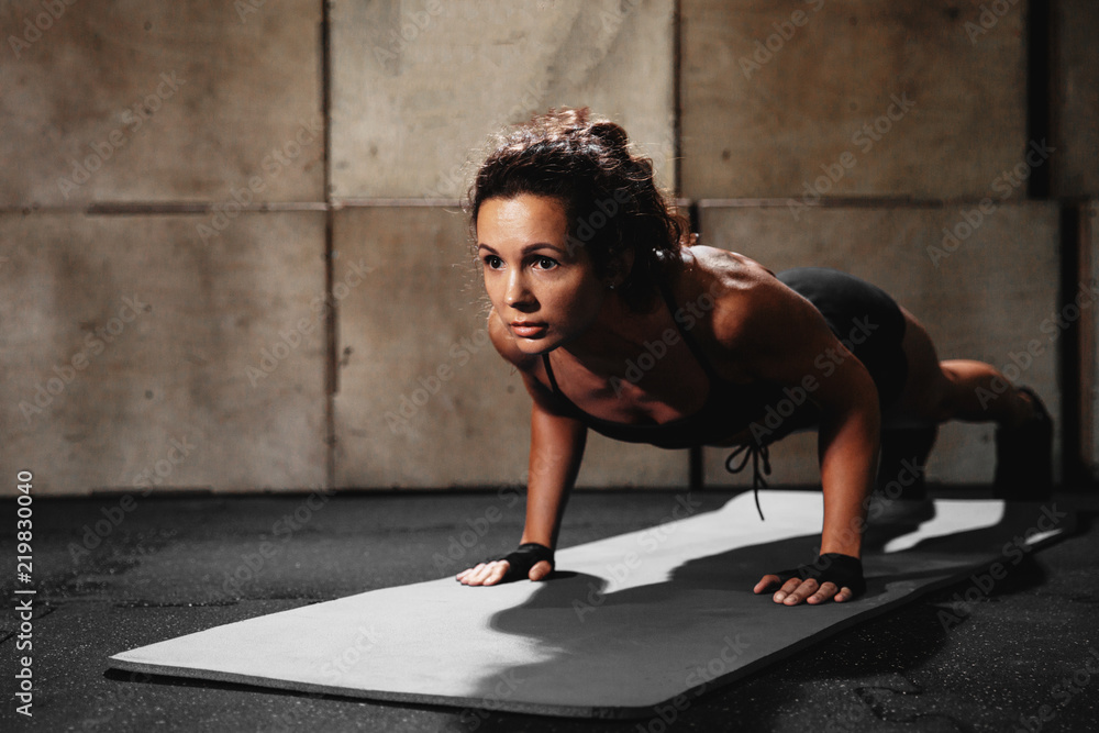 Shot of young woman doing push-ups at the gym. Strong female athlete doing pushups on exercise mat at gym. Female exercising on fitness mat at gym.