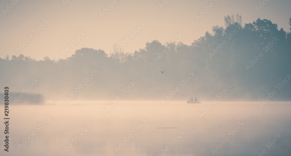 Fototapeta premium Foggy river at beautiful early autumn morning. Fishermans in the rubber boats and seagull flying over.