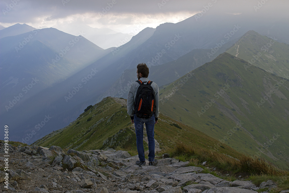 A male mountaineer looking over a vast, rocky, mountainous sunrise scene.