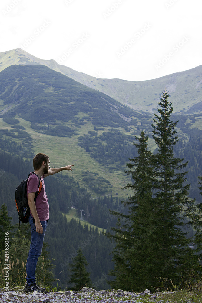 a man in a T-shirt stands sideways and shows the way to the mountains, Move forward, way up