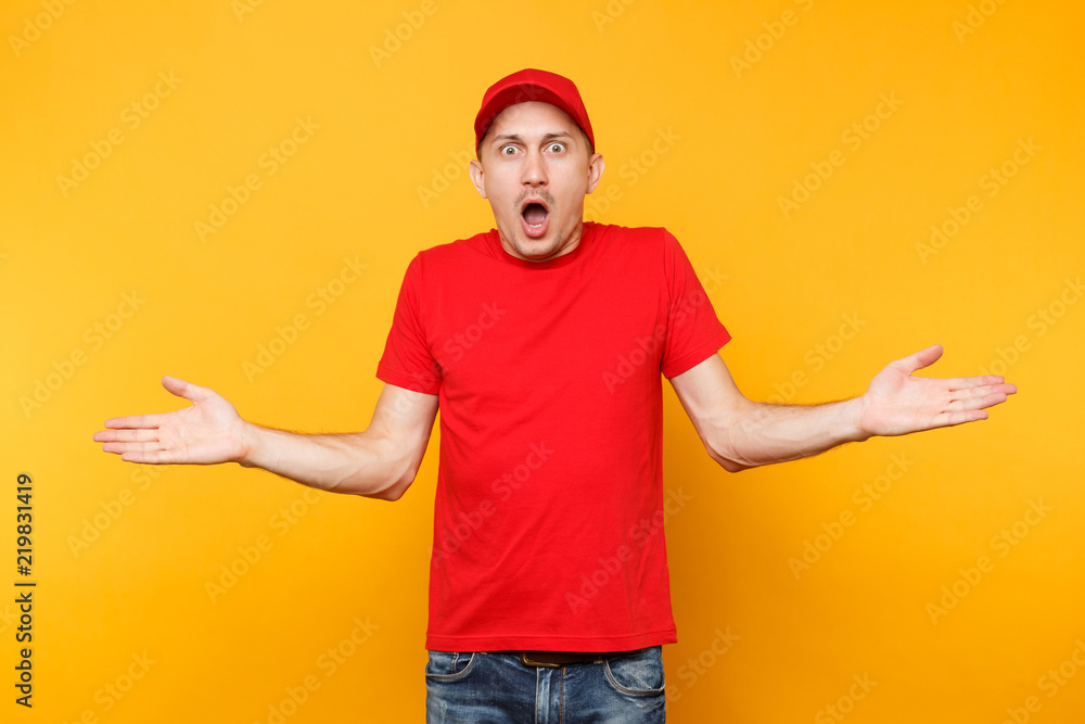 Delivery upset man in red uniform isolated on yellow orange background. Professional sad shocked male employee in cap, t-shirt working as courier or dealer spreading hands. Service concept. Copy space