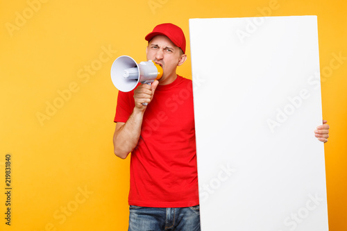 Delivery service man isolated on yellow background. Male employee courier in red cap, t-shirt screaming in megaphone hot news, hold big white empty blank billboard. Fun guy announces discounts sale.