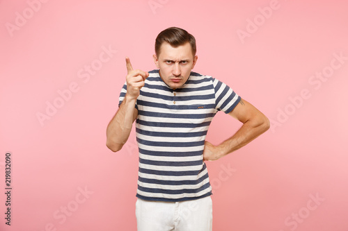 Portrait of severe cruel brutal young man in striped t-shirt poining index finger up isolated on trending pink background. People sincere emotions lifestyle concept. Advertising area copy space.