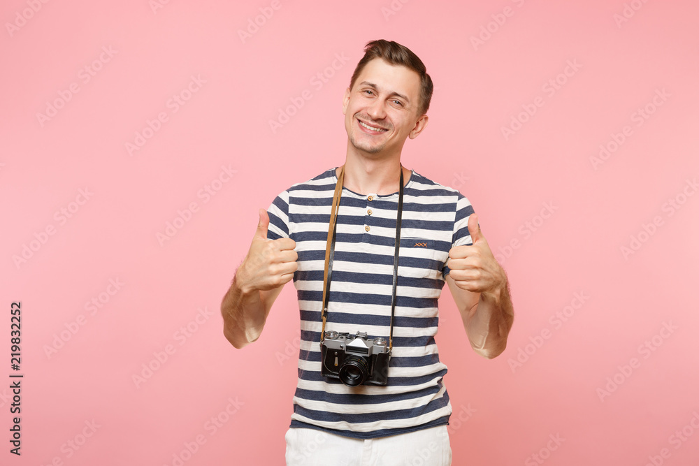 Fototapeta premium Portrait of smiling young photographer man wearing striped t-shirt take pictures on retro vintage photo camera isolated on trending pastel pink background. People sincere emotions lifestyle concept.