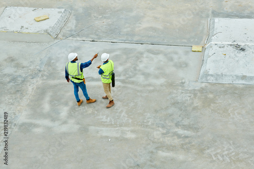 Top view portrait of two workers standing on concrete floor of construction site and planning project, copy space background