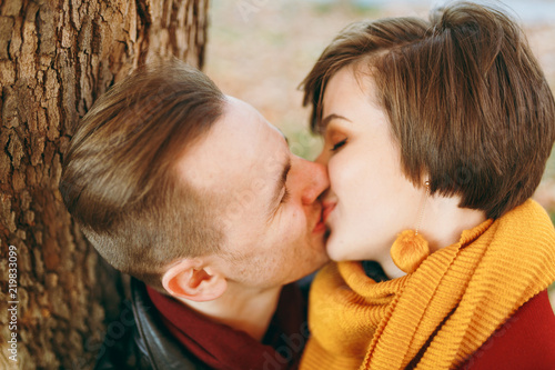 Portrait of Young happy beautiful couple in love smiling woman man with closed eyes kissing in autumn city park outdoors on fallen leaves background. Love relationship family people lifestyle concept. © ViDi Studio