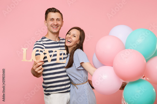 Portrait of couple hold wooden word letters love. Woman and man in blue clothes celebrating birthday holiday party on pastel pink background with colorful air balloons. People sincere emotions concept