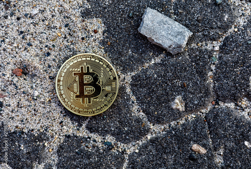 lonely bitcoin coin thrown on asphalt road next to a large stone