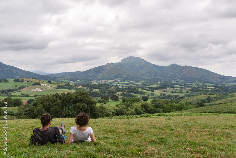 Pareja joven descansando en lo alto de una colina verde y mirando a un bonito paisaje montañoso. Pirineos, España.