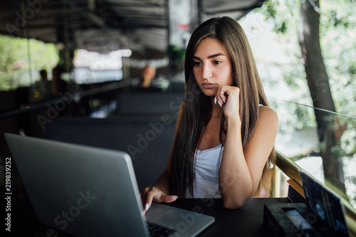 Portrait of a young beautiful women enjoying coffee during work on portable laptop computer. Charming female student using net-book while sitting in cafe bar interior during morning breakfast