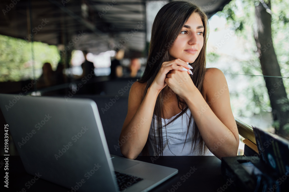 Portrait of a young beautiful women enjoying coffee during work on portable laptop computer. Charming female student using net-book while sitting in cafe bar interior during morning breakfast