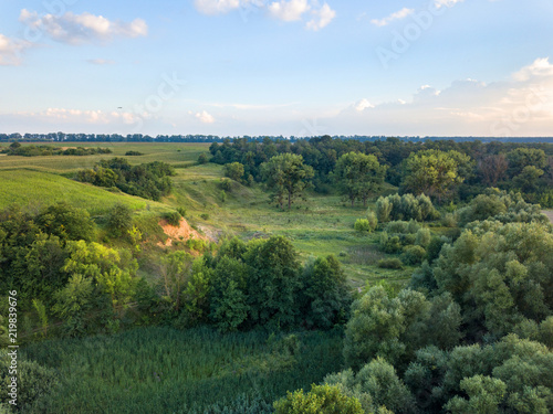 Aerial view from the drone of a natural landscape with greenery, forest, field, ravine on a background of a cloudy sky.