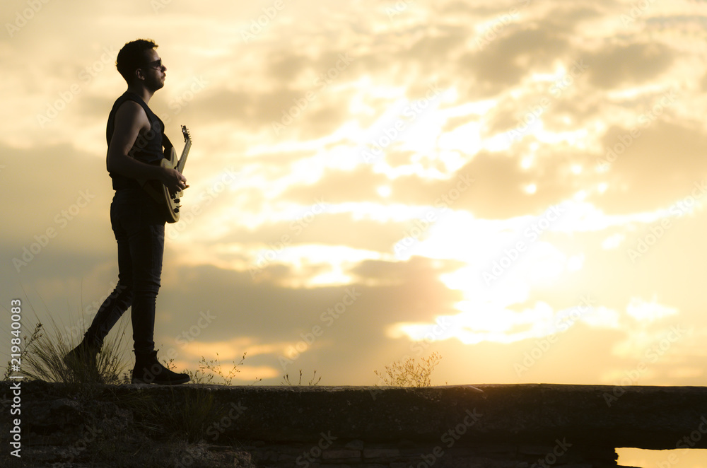 Man performs on electric guitar on old Roman aqueduct during sunset.