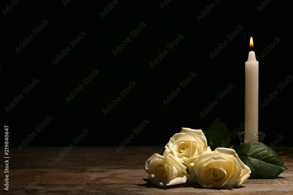 Fototapeta premium Piękne białe róże i świeca na stole na czarnym tle. Symbol pogrzebu