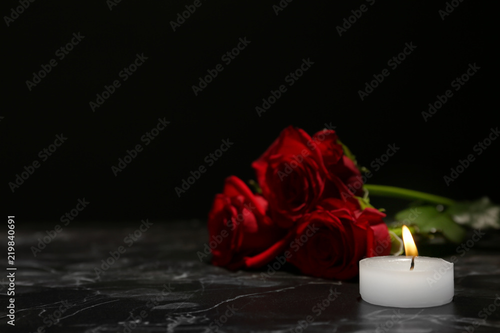 Fototapeta premium Piękne czerwone róże i świeca na stole na czarnym tle. Symbol pogrzebu