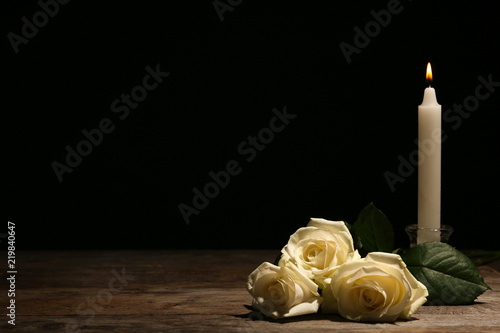 Beautiful white roses and candle on table against black background. Funeral symbol