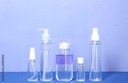 Different cosmetic bottles on table against color background