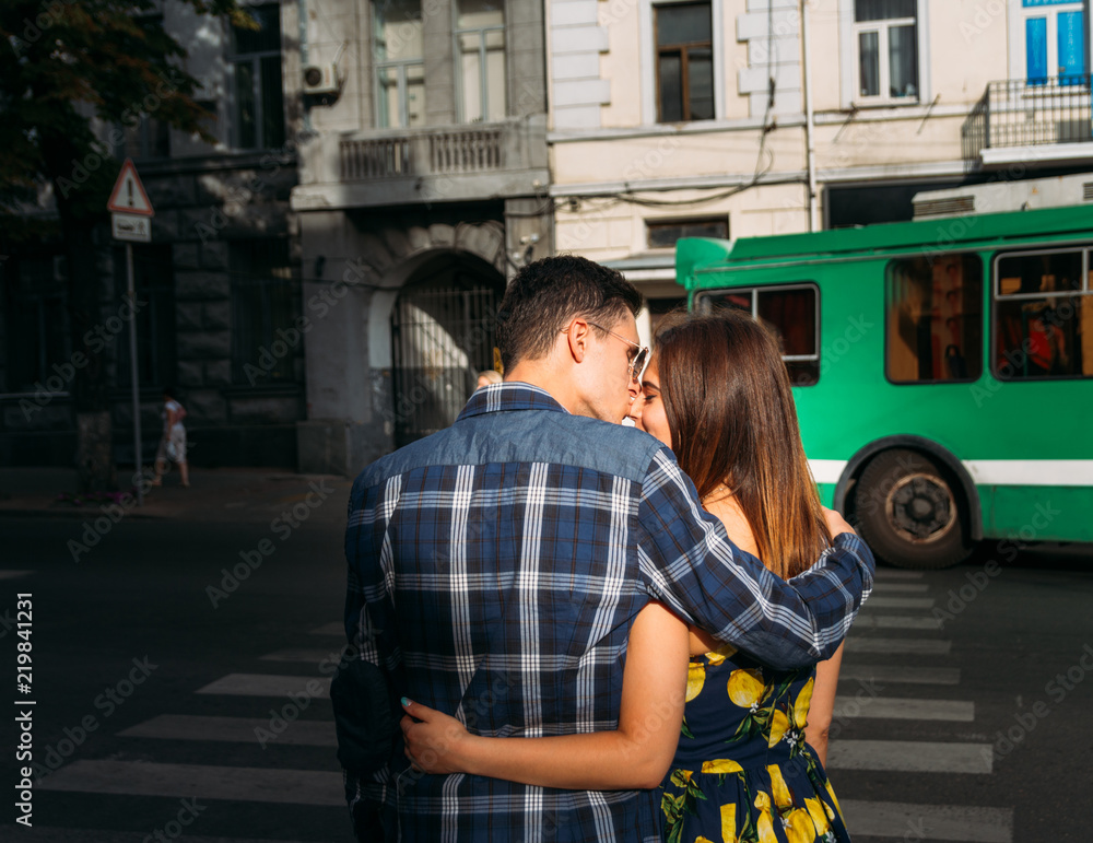 at the pedestrian crossing a guy kisses a girl in the nose and hugs