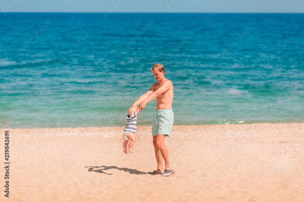 Young happy father playing with his baby at the beach