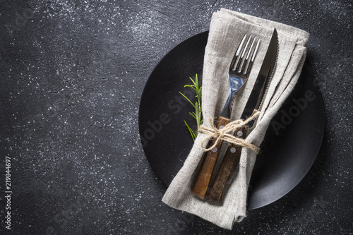Black plate, cutlery and napkin on stone table top view.