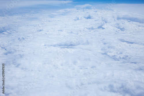 Airplain window seat view of big white thick fluffy clouds with a clear blue sky at the background