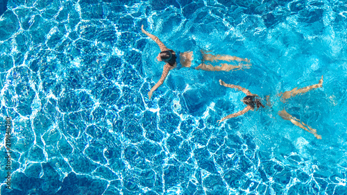 Aerial top view of girls in swimming pool water from above, active children swim, kids have fun on tropical family vacation, holiday resort concept 