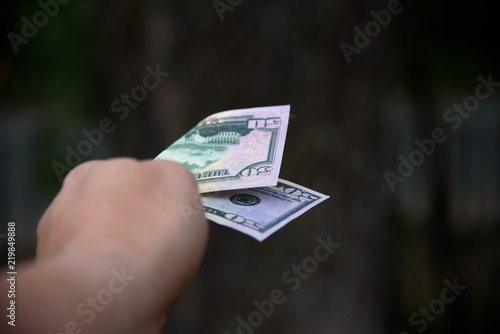 Dollar bill in the outstretched male hand on a green nature background