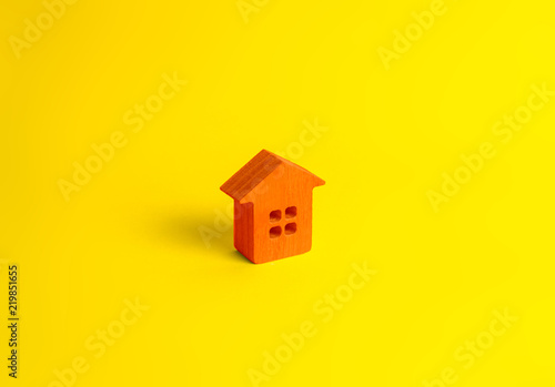 A small orange wooden house stands on a yellow background. The concept of buying and selling real estate, renting. Search for a house. Affordable housing, credit and loans. Investments in business