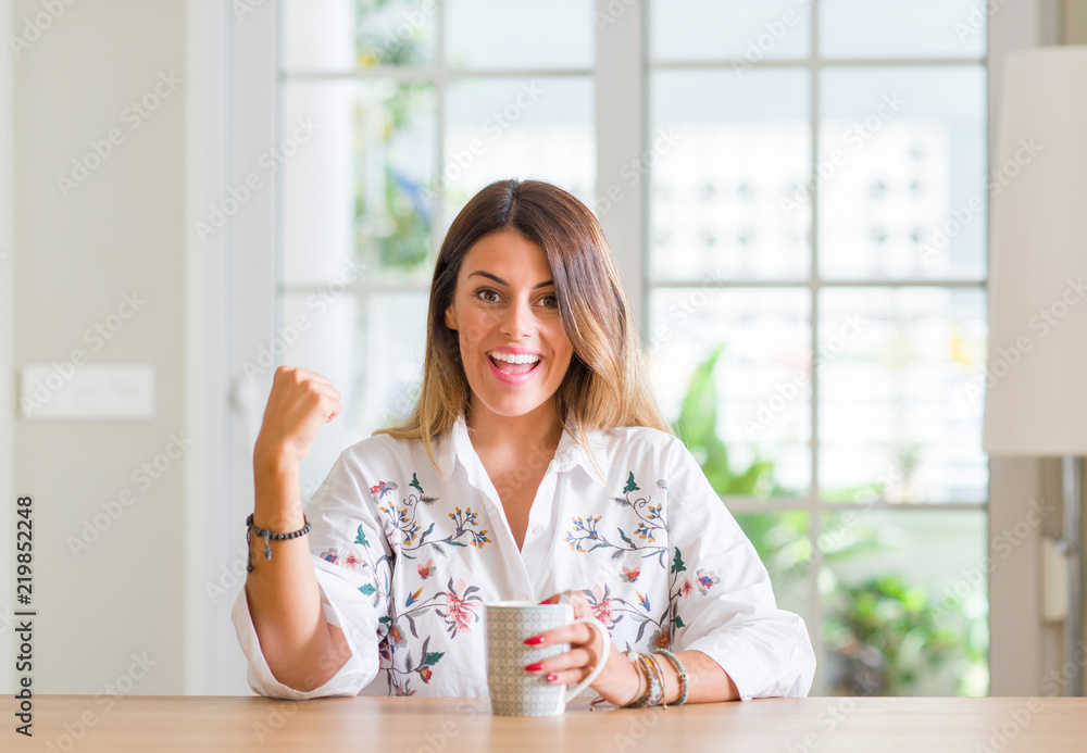 Young woman at home drinking coffee screaming proud and celebrating victory and success very excited, cheering emotion Young woman at home drinking coffee screaming proud and celebrating victory and success very excited, cheering emotion