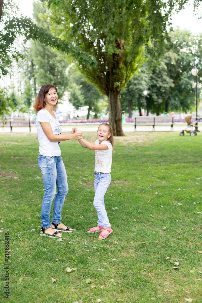 Obraz premium daughter and mother spinning on the lawn.in a white t-shirt and jeans. a walk in the Park. child. mother-daughter. summer.