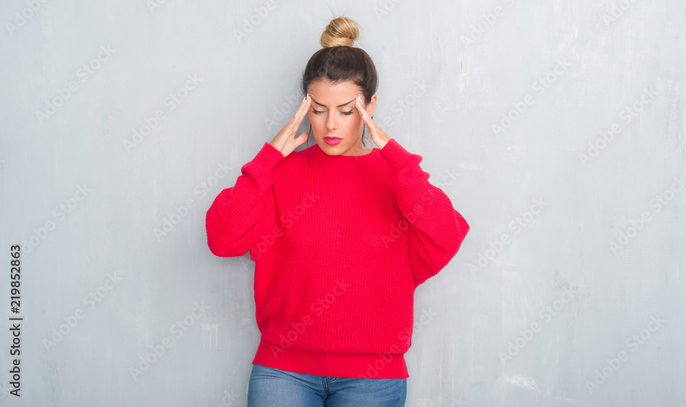 Young adult woman over grey grunge wall wearing winter outfit with hand on head for pain in head because stress. Suffering migraine. Young adult woman over grey grunge wall wearing winter outfit with hand on head for pain in head because stress. Suffering migraine.