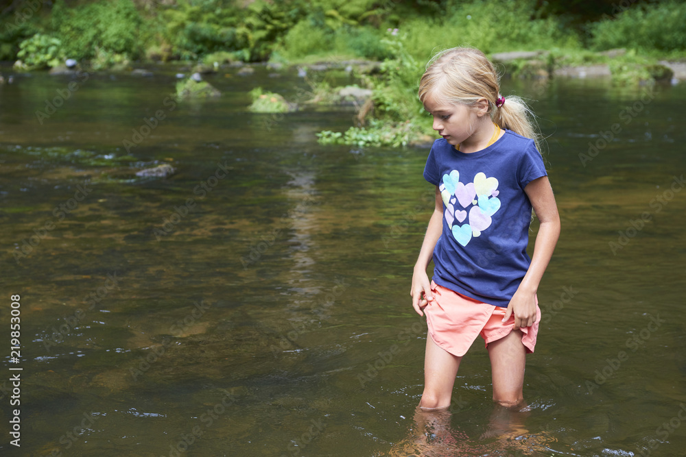 Naklejka premium Child cute blond girl playing in the creek. Girl walking in forest stream and exploring nature. Summer children fun. Children summer activities