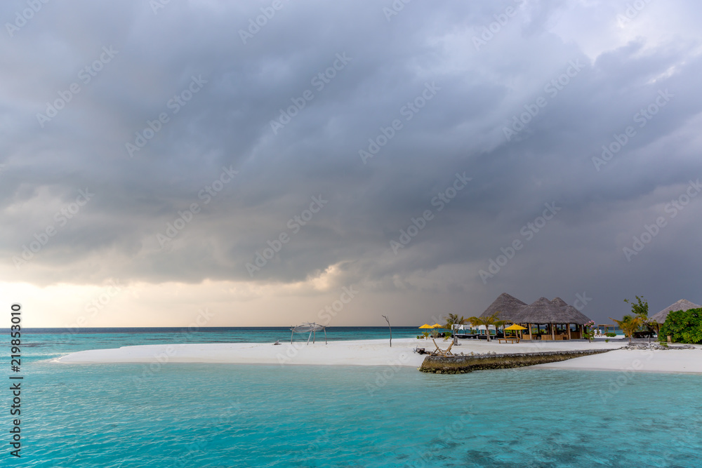 An idyllic island in Maldive in a stormy weather afternoon. Super clear water, white sand, traditional huts and tropical climate feeling.